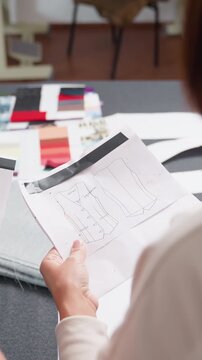 studio table pattern sheets and fabric swatches, designer and assistant reviewing sample pattern, measuring marks visible, pencil and color cards on table, quiet collaborative mood in atelier