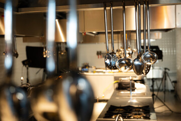 Stainless steel ladles and a skimmer are hanging prominently in the foreground, showcasing essential tools used in a busy professional kitchen with blurred shelves of equipment in the background