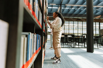 Female student laughing and looking at books on bookshelves in surprise © Drobot Dean