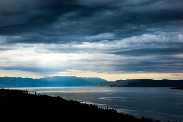 Moody sea landscape under dramatic storm clouds along a rugged coastline, with soft light breaking through the sky. This atmospheric view is ideal for travel ads and wide web banners.