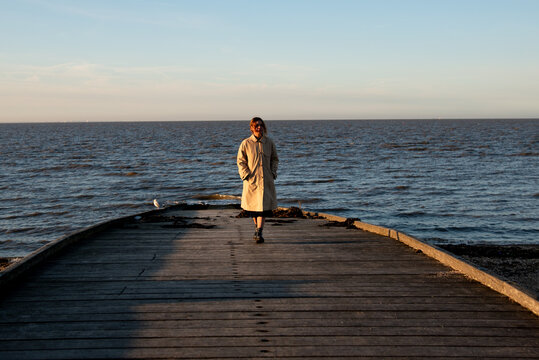 Woman in trench coat walking on wooden pier, enjoying quiet solitude by the sea