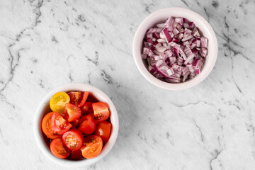 chopped cherry tomatoes and diced red onion prepared for cooking on a marble background