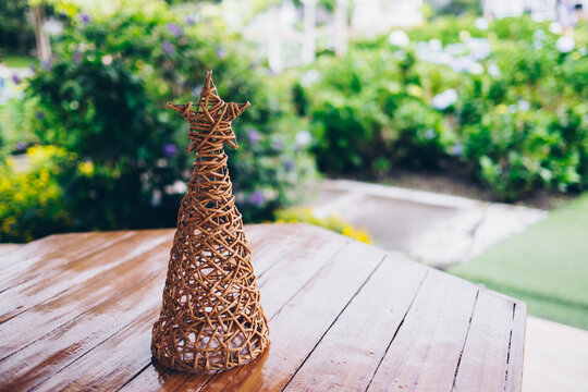 Handcrafted woven Christmas tree made from strong rattan material on wooden table in the garden. Selective focus. Copy space.