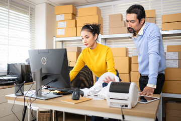 Business owner and employee labeling packages using printer and tablet in warehouse office