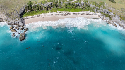 aerial landscape view of an abandoned tropical beach with palms, white sandy beach, big waves and turquoise water surrounded by rocky cliffs, somewhere in the Caribbean region 