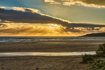 Sunbeams illuminate the ocean and sandy beach at golden hour