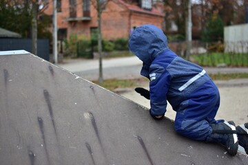 Toddler boy climbing up skate ramp in playground during autumn. Child wearing winter clothes developing strength, balance and coordination through active outdoor play and early childhood learning