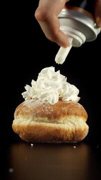 Donut topped with whipped cream shown in close-up under soft light on black background with cream forming layered structure