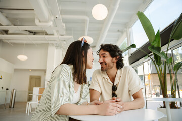 Fototapeta premium Man laughing and listening to woman talking while they hold hands and sit at a table