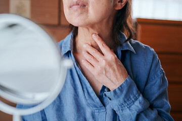 首のシワを鏡で確認するシニア女性