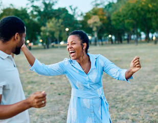 Happy young black couple, portrait of a beautiful woman with her husband dancing or swinging and holding hands in park outdoors