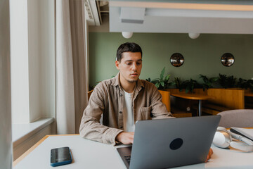 Naklejka premium Male worker typing on laptop while looking at it and sitting at desk