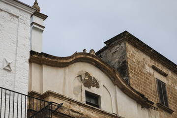 Fototapeta premium baroque facade architecture detail featuring weathered stone, peeling stucco, and curving ornamentation, set against a pale sky, evoking the rustic charm of southern italy.
