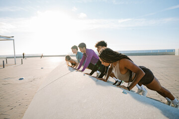 A group of five athletes stand and do push-ups next to each other