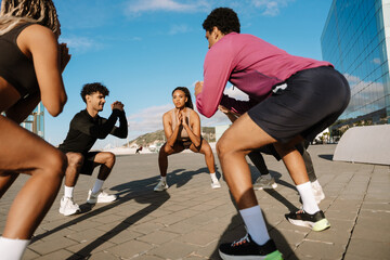 A group of four athletes squat in a circle and hold their hands together in front of them