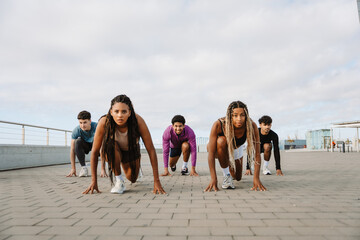 A group of five athletes look intently ahead as they stand in a starting position for a run