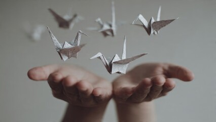 Hands releasing origami paper birds of hope minimalist studio setting symbolizing letting go