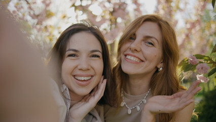 Fototapeta premium Two friends smile and takes a selfie together in a garden filled with pink flowers during a sunny afternoon in spring