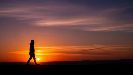 Fototapeta premium Vibrant sunset paints the sky as a solitary figure walks along the horizon, symbolizing a journey, new beginnings, or tranquil reflection