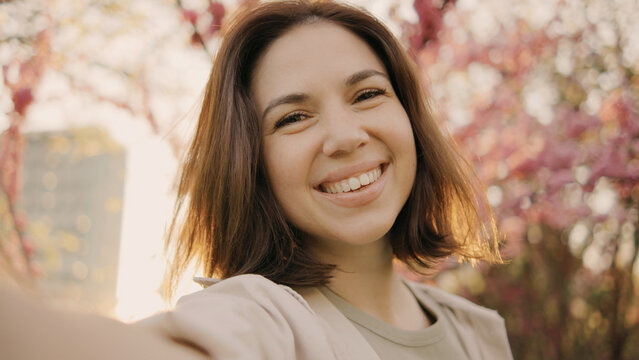 Smiling woman takes a selfie in spring with blooming flowers and cityscape in the background during golden hour - Powered by Adobe