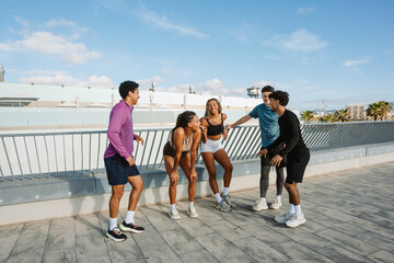 A group of five athletes stand and laugh while talking, four of them leaning on the railing