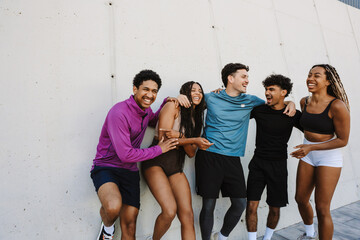 Fototapeta premium A group of five athletes laugh and hug while standing and leaning on a wall