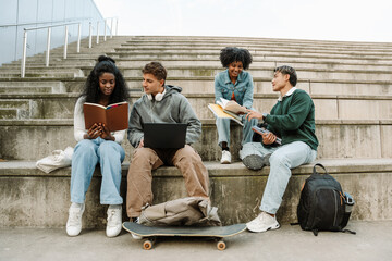 A group of four students sit on the bleachers in pairs while three of them read books and one talks