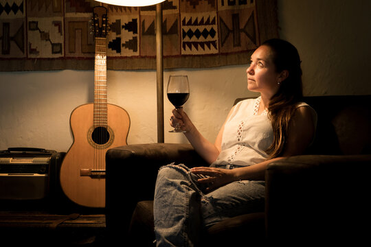 Mujer tomando vino en la intimidad de su casa bajo la tenue luz de una l&aacute;mpara, relajada y pensativa