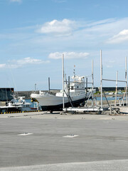 Fototapeta premium Fishing boat undergoing maintenance on a dry dock in a sunny harbor with blue sky and clouds