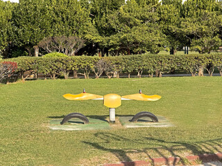 Yellow seesaw playground equipment with tires in a grassy park on a sunny day