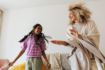A mother and her daughter dance and laugh while looking at each other