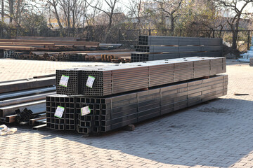 Outdoor view of stacked square and rectangular steel hollow section profiles with labels stored in...