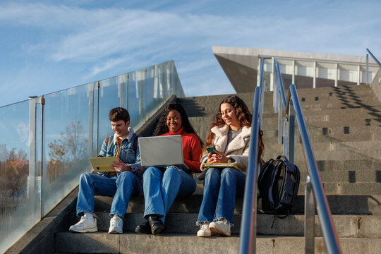 Diverse college students are studying and using technology on university steps outdoors