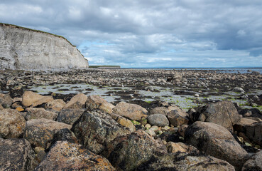 Rocky beach at Silverstrand, Galway, Ireland with a large cliff, partly cloudy sky, and calm sea, showcasing natural beauty and geological features