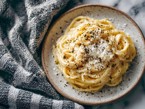 Minimalist overhead shot displays cacio e pepe pasta on a ceramic plate with a generous dusting of black pepper on a marble table.