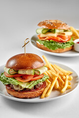 A classic bagel sandwich filled with smoked salmon, cream cheese, lettuce, cheese, and cucumber, served on a white plate against a bright white background with strong shadows.