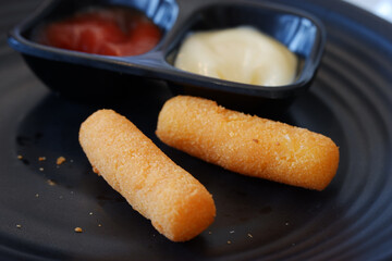Delicious fried mozzarella stick appetizer on black plate. This crispy snack with ketchup and mayonnaise sauce popular junk food meal, perfect for party