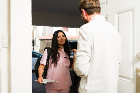 Caregiver showing identification badge to man at front door, offering home visit healthcare service - Powered by Adobe