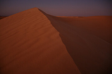 Minimalist desert landscape featuring sharp sand dune ridge illuminated by warm sunset light. Sahara desert near Siwa oasis in Egypt