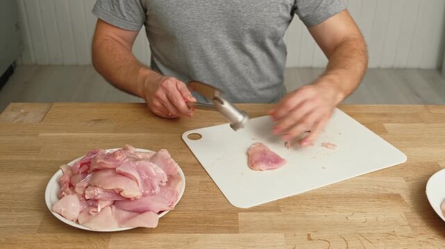 Person using meat tenderizer on raw chicken. Chef preparing pork loin slice with meat mallet on cutting board. Man tenderizing fillet. Cooking cutlets pounding poultry breast close-up. Culinary dish.