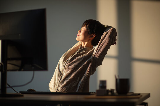 Japanese nonbinary professional doing a side-bend stretch in a sunlit office. Inclusive workplace wellness with modern d&eacute;cor. Nonbinary person stretching, wellbeing at work. Asian person.