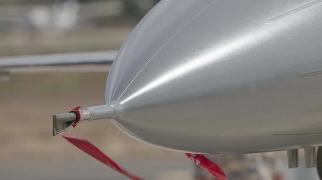 Military transport aircraft nose section featuring pitot static probe with protective cover and red remove before flight streamer attached during ground operations