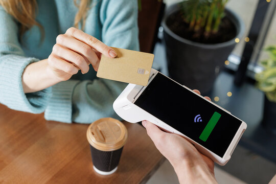Customer taps bank card on handheld POS terminal for contactless payment in cafe