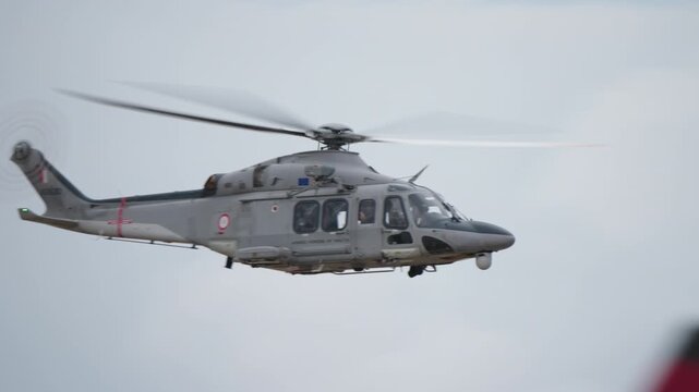 Twin-engine medium utility helicopter with main rotor and tail rotor visible hovering sideways in clear blue sky