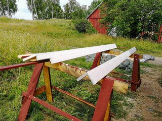 Wooden boards, painted white, lie on sawhorses to dry. Exterior repair work on a wooden house