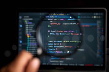 Close-up view of a computer screen with colorful JavaScript code magnified by a handheld magnifying glass, symbolizing debugging, software development, and error tracking in programming tasks.