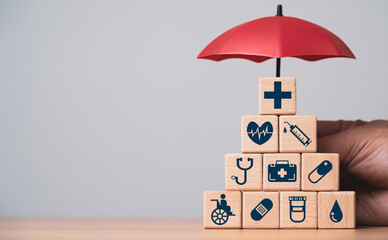 Wooden blocks with medical icons in a pyramid under a protective umbrella for health insurance life protection medical coverage wellness support safety and long term healthcare security concept.