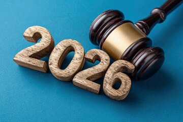 A striking composition features a classic wooden gavel with brass details positioned next to the prominent wooden numerals '2026.' The elements rest on a vibrant, textured blue surface, creating a pow