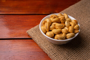 Close-up of bowl of roasted cashew nuts on burlap and wooden table, healthy snack food rich in protein and nutrition