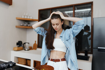 Frustrated young woman in a kitchen, struggling with meal preparation, wearing a casual outfit and expressing emotions of stress and concern